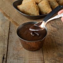 Getting a spoonful of tamarind and date chutney out of a small container