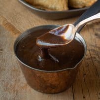A spoon inside a small pot of tamarind and date chutney