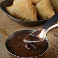 Serving a spoonful of tamarind date paste with samosa in the background