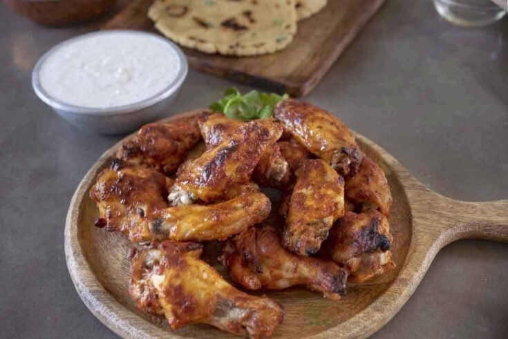 Tandoori masala chicken wings on a serving board with raita