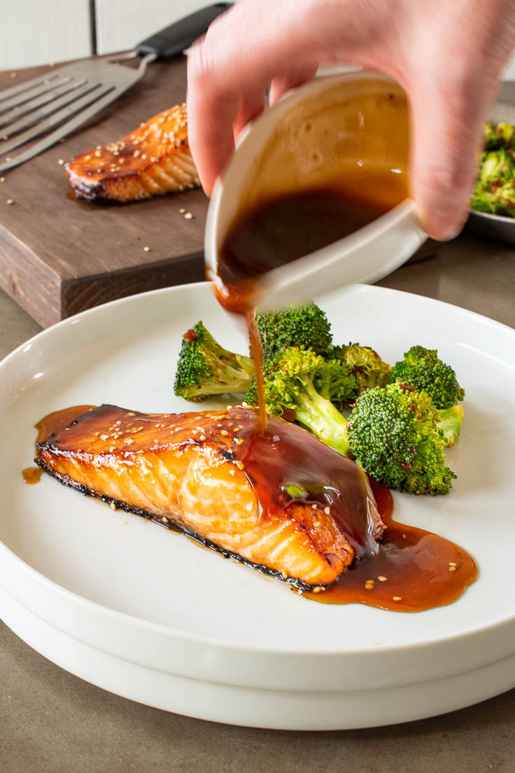 Pouring teriyaki sauce over salmon on a white plate with broccoli