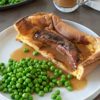 1 toad in the hole sausage inside batter on a white plate with peas and onion gravy