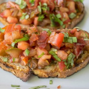 A closeup of tomato bruschetta topped with crispy prosciutto