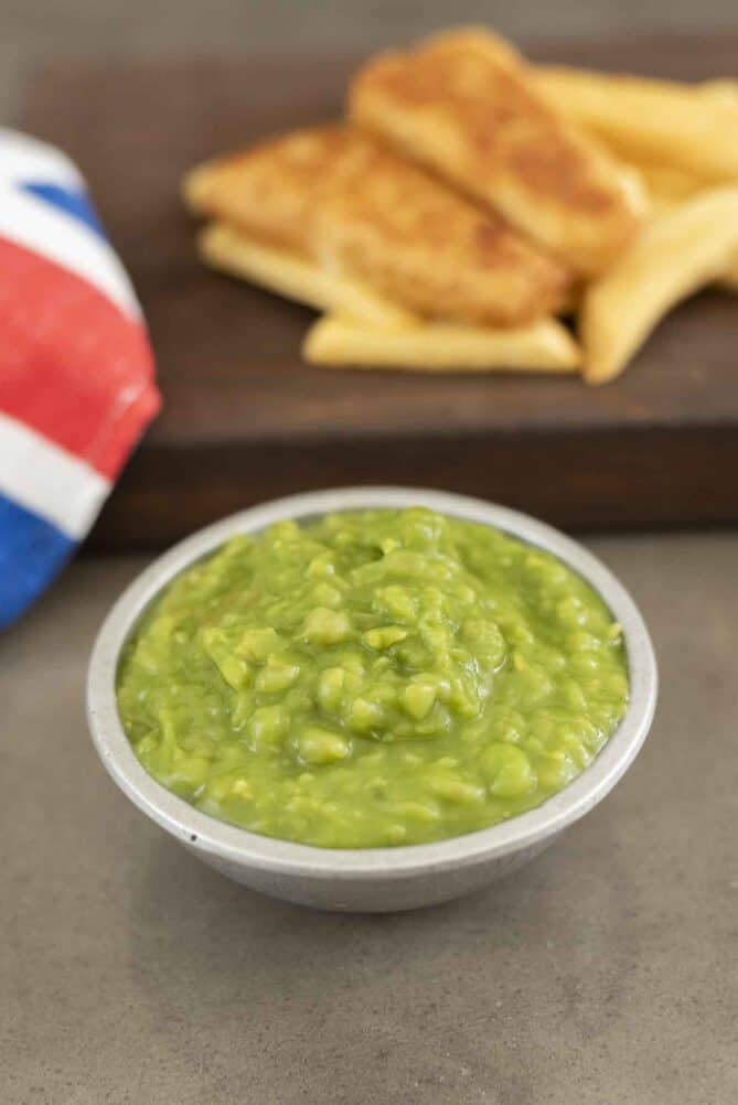 Mushy peas in a silver bowl with fish and chips in the background