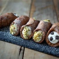 5 cannoli on a board dusted with powdered sugar