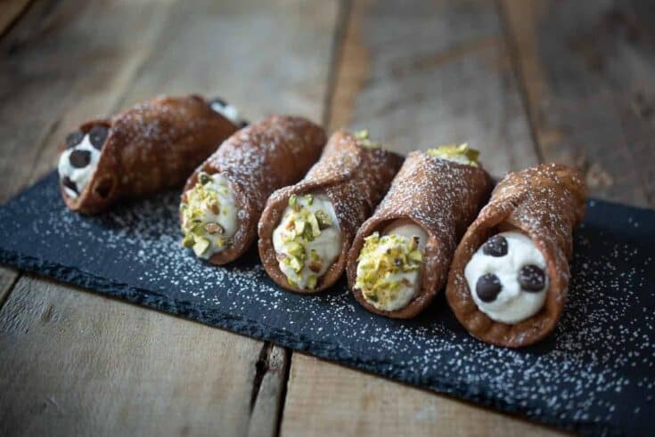 5 cannoli on a board dusted with powdered sugar