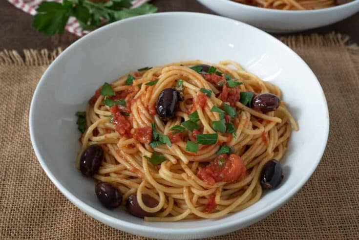 Shiny black olives, tomato and parsley with spaghetti in a white bowl