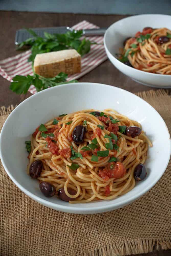A bowl of spagehetti with tomato sauce, olives and capers