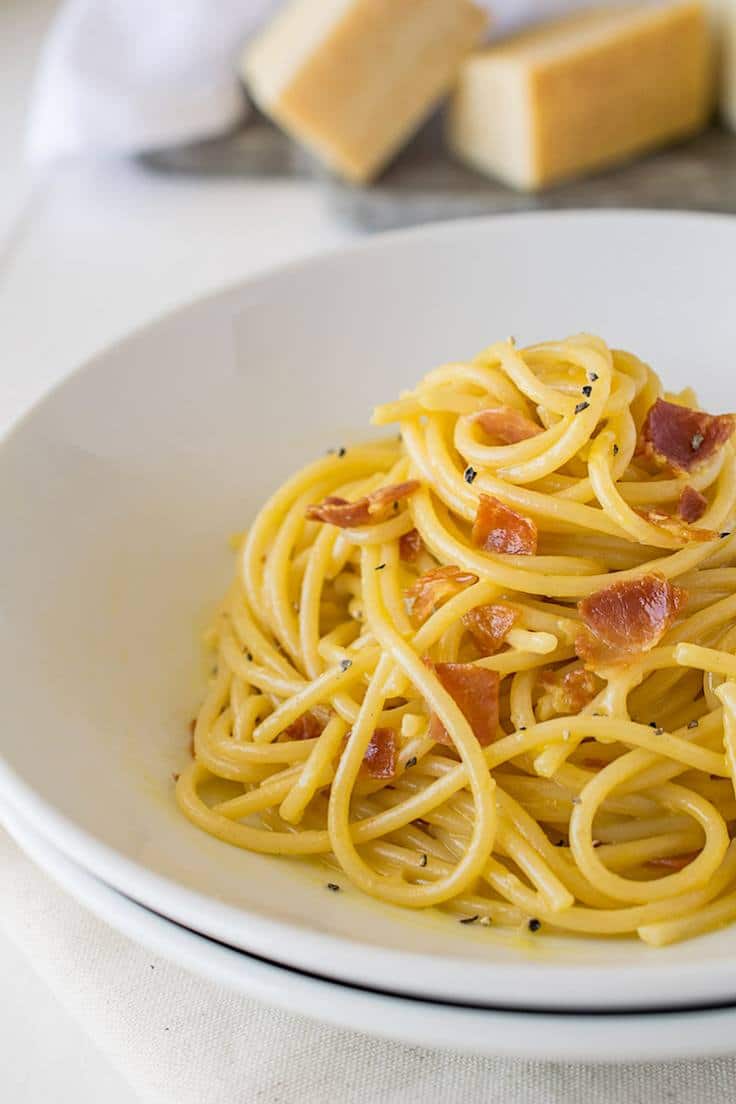 A closeup of Traditional Spaghetti Carbonara in a white bowl showing the creaminess and pancetta pieces