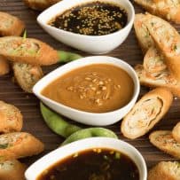 3 white teardrop bowls of Asian dipping sauces