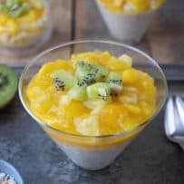 Tropical rice pudding in a coned shape glass topped with fresh mango, kiwi and pineapple with a spoon and extra kiwi