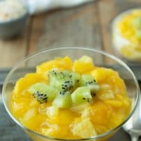 Bright orange and yellow mango and pineapple in a glass with rice pudding with chopped kiwi