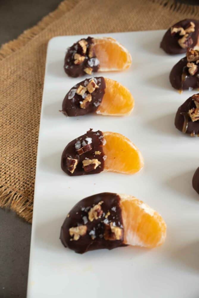 A closeup of orange pieces half covered with chocolate, pecans, flaky sea salt