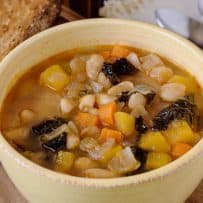 A hearty Tuscan bean soup with Cannellini beans, yellow squash, carrot and kale in a bowl