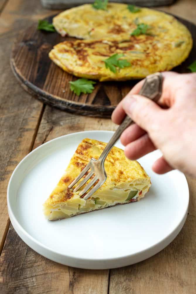 Cutting a bite with a fork from a slice of vegetable Spanish omelette tortilla