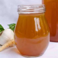 A jar full of vegetable broth with fresh vegetables