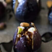 A fresh fig cut open and filled with goat cheese, pistachios and topped with balsamic glaze
