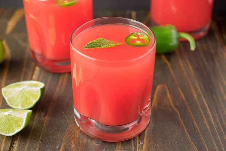 A vibrant watermelon colored drink with green mint and jalapeño slice floating on top