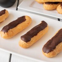 4 eclairs lined up on a plate with more in the background