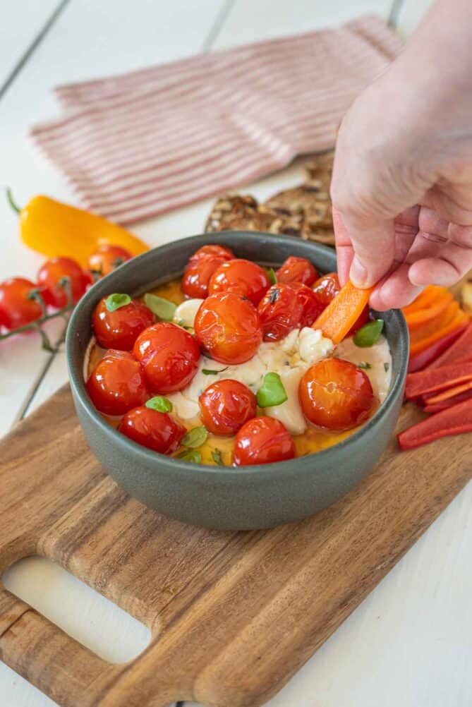 Dipping a sweet pepper into cheese dip with confit tomatoes