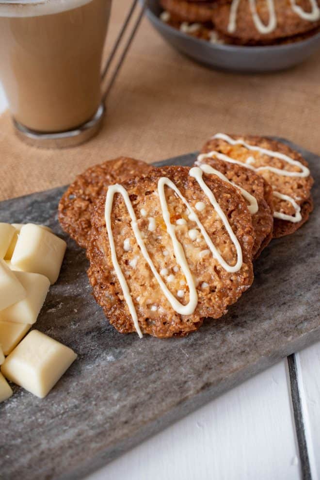 4 white chocolate Florentine cookies on a grey board with a latte