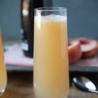 A side view of a tall glass filled with white peach Bellini