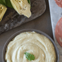 A bowl of creamy artichoke dip garnished with a basil leaf.