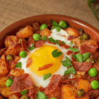 A perfect sunnyside up egg in the center of potatoes, peas and ham cooked in tomato.